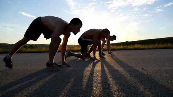 一群运动员在比赛前蹲在起跑线上一起奔跑三个肌肉发达的年轻人在短跑起点日落时分人们站在乡村公路的起跑线上缓慢的运动