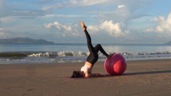 健康的亚洲美女早上在海滩上用球做瑜伽练习