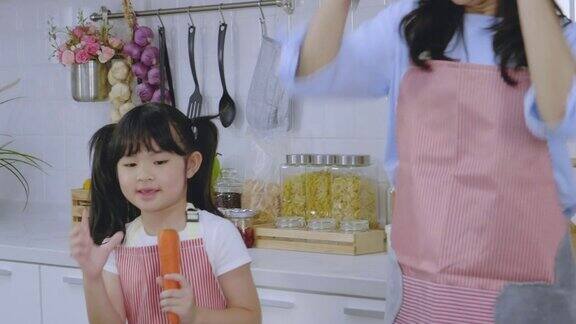 亚洲家庭的母亲和女儿一起随着音乐跳舞在家里的厨房里享受煮早餐健康保健的日常活动理念