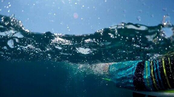 水下慢动作:一个年轻的冲浪者在开放水域的海浪上划桨