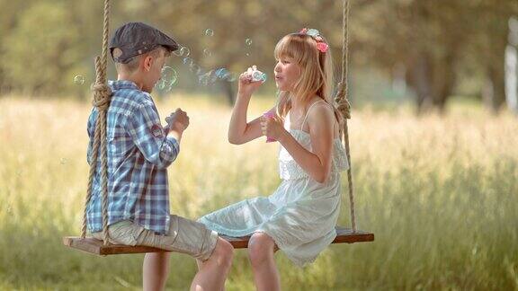 一个小女孩和一个小男孩坐在秋千上吹泡泡