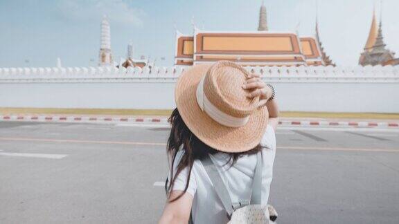 开朗的年轻亚洲女子牵着男友的手在曼谷的佛寺旅游