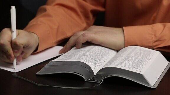 一个人坐在桌子旁读圣经引导手指沿着线把重要的想法写在一张纸上特写镜头