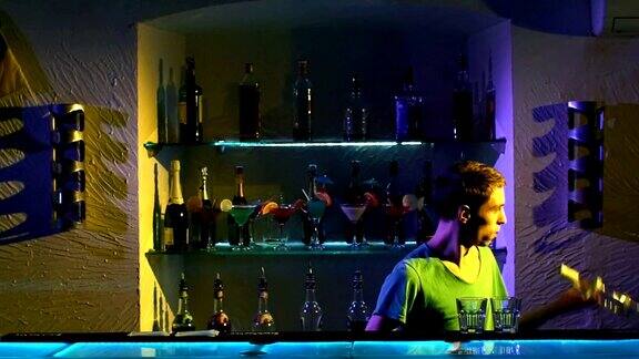 年轻的酒保拿着两个玻璃杯和酒瓶站在吧台后面慢动作表演