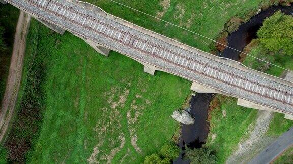 鸟瞰拱门石桥上的铁轨飞机就在桥的上方在田野和森林之间的石头高架桥上的一对铁路牧场上的奶牛镜头向前移动版本10
