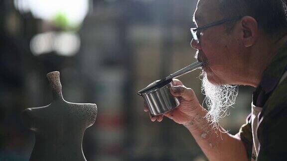 亚洲华人高级泥塑艺术家在雕塑家身上吹颜料在他的工作室里用纺纱陶轮工作