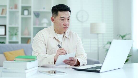 集中亚洲人观看视频电话课程或培训而坐在家里的办公室使用笔记本电脑