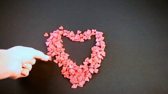 女人的手把心形的小糖果放在情人节的木桌上