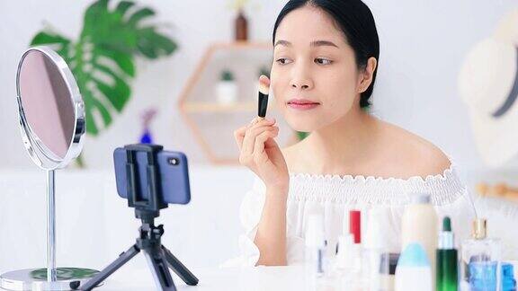 美丽的亚洲女人博客展示如何化妆和使用化妆品在智能手机前录制视频直播在家商业在线影响者对社交媒体