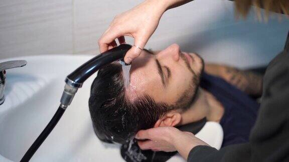 女士用洗发水按摩头发顾客男士在美容院洗头理发师洗头快乐的白种人享受服务在理发店