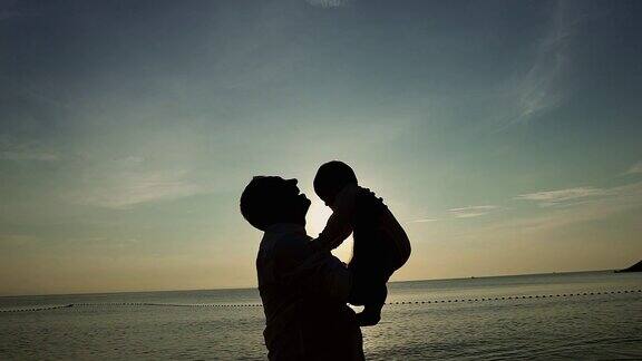 家庭在海滩概念白人父亲玩和抱着他的儿子在热带海滩上的日落