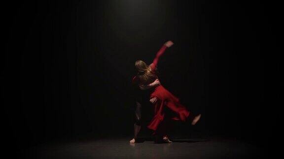 在一个黑暗的演播室里女人和男人在聚光灯下的黑色背景上与支架一起跳舞慢动作