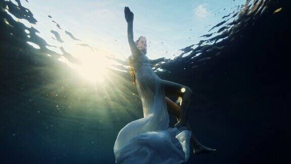 日落时一名身穿白色连衣裙的年轻女子在海里游泳