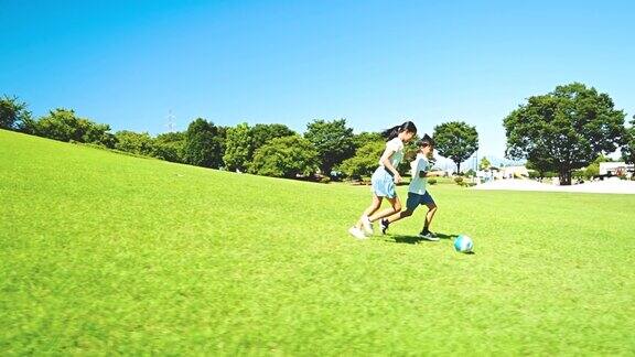 亚洲孩子在蓝天下的公园里踢足球