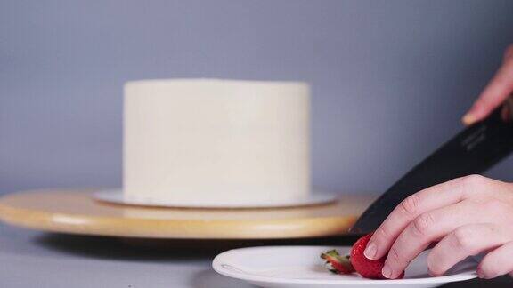 年轻女子用手把草莓切成两半装饰蛋糕