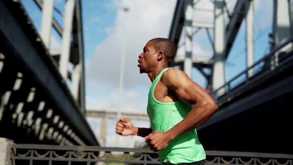 腰部以上跟踪左慢动作镜头的年轻非洲运动员呼吸正确而跑下城市大桥