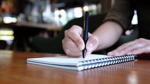 一个女人的手正在咖啡馆的木桌上一本白纸笔记本上写着什么