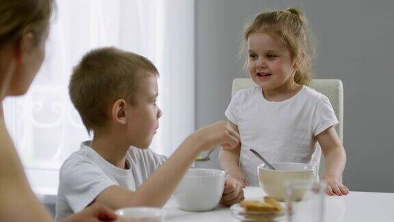 可爱的女孩在早餐时与妈妈和哥哥聊天