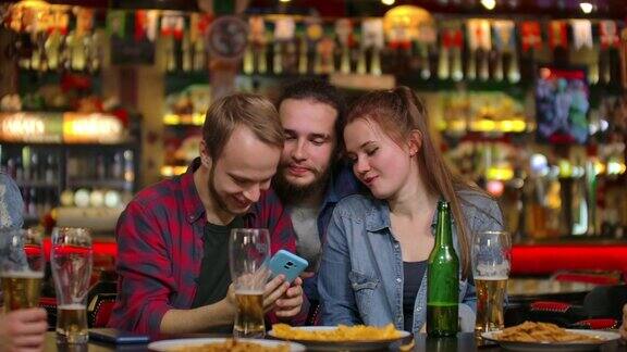 朋友们在酒吧用智能手机自拍年轻人在摆姿势有说有笑啤酒瓶朋友们正在用智能手机自拍