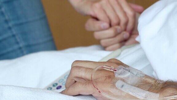 在医院病床上一名妇女牵着丈夫的手丈夫的手臂上还放着静脉注射针
