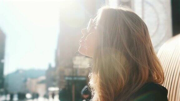 一个金发女孩在明亮的夏日阳光下晒太阳在街道上背景是一个繁忙的城市特写时尚