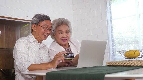 幸福的亚洲老年夫妇使用笔记本电脑和支付与信用卡在家里家庭放松和花时间在一起在家里退休人士和生活方式