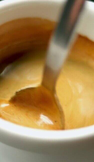 用金属茶匙将热黑特浓咖啡和蓬松的泡沫混合在一个白色咖啡杯里