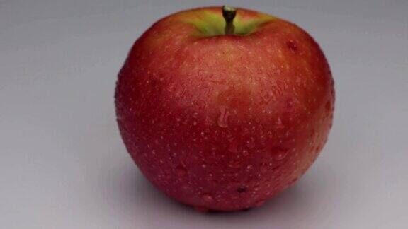 在白色背景上的露珠中旋转一个红苹果