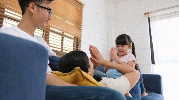 亚洲女孩的女儿和她的父母在沙发家玩幸福的家庭观念