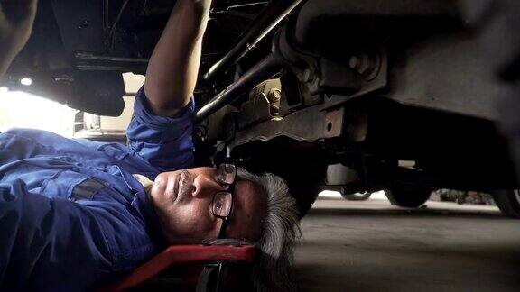 从车轮近侧视图:亚洲高级汽车技师在车辆下工作