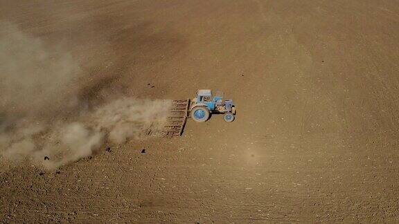 空中滑拍农民在蓝色拖拉机上犁地尘土和干旱的土壤农业在春天