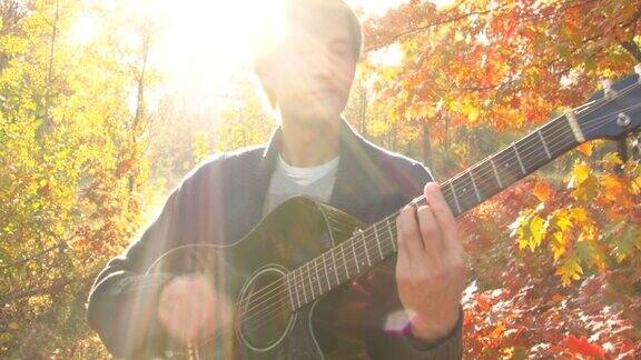 年轻的金发男子在秋天的森林里弹吉他
