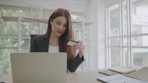 美丽的年轻亚洲女商人在办公室用她的笔记本电脑在网上购物