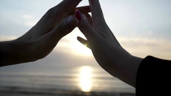 慢镜头中海滩上夕阳下的手拉手做成心形的剪影