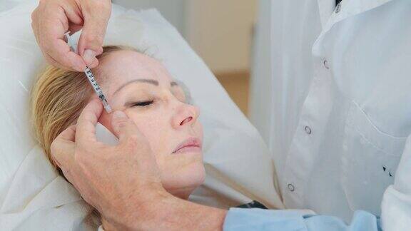 整形外科医生用餐巾清洁面部并在客户的眼部区域用注射器进行面部肉毒杆菌注射