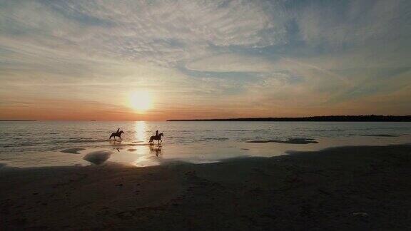 两个女孩在海滩上骑马马在水上跑在这张航拍照片中可以看到美丽的日落