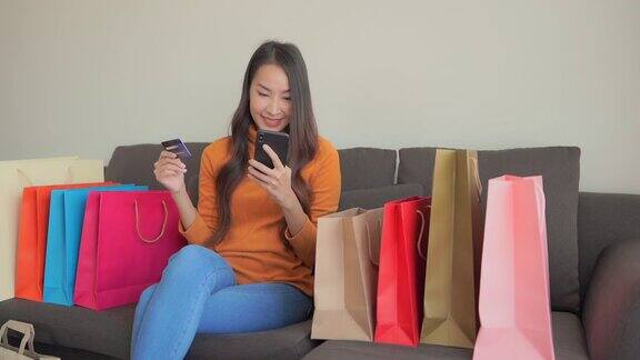 年轻的亚洲女性使用笔记本电脑或手机或信用卡在网上购物