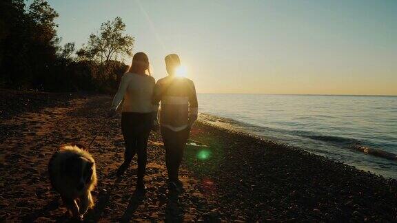 日落时分在海边遛狗一对多民族的夫妇正沿着海岸散步