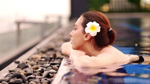 亚洲年轻女子放松在豪华酒店温泉游泳池享受美丽的日落近距离观察女性在城市酒店享受夏季旅行