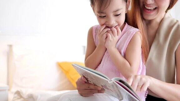 年轻的亚洲母亲在卧室里给女儿读童话故事