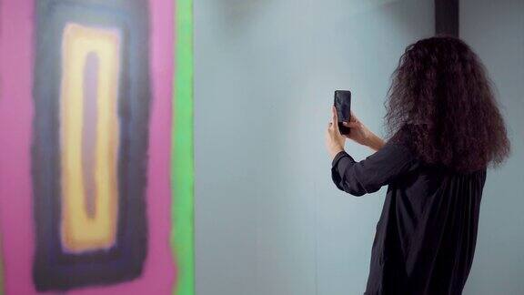 一位黑发女子正在用智能手机拍摄一幅抽象画