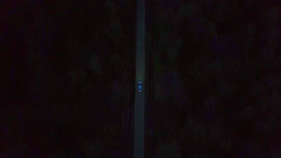 鸟瞰图银色商务轿车凯迪拉克Cts行驶在黑暗的乡村道路之间的森林在晚上从无人机看白色汽车氙气前灯行驶在夜晚的道路通过黑暗的森林