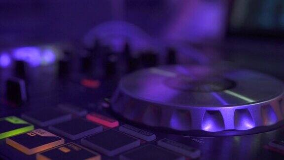 DJ控制器混合音乐在夜间派对和在迪斯科俱乐部的彩色灯光关闭DJ混音播放器和音响控制台的迪斯科派对唱片骑师控制台和混合甲板与彩色照明