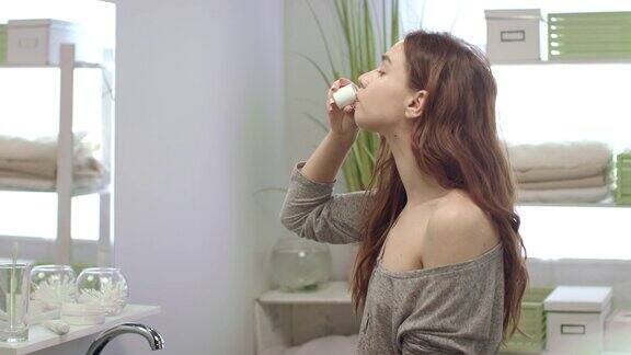 年轻女子用牙齿漱口漱口在浴室的镜子