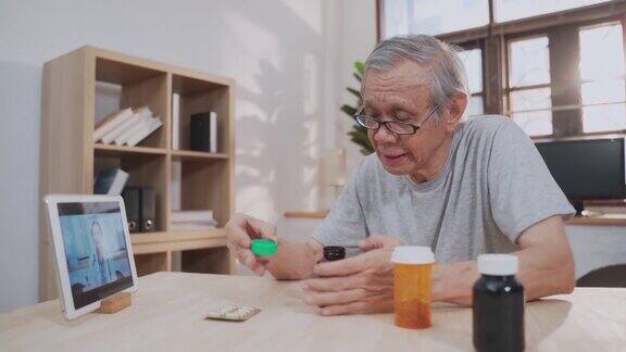 远程医疗的亚洲老年男性患者使用笔记本电脑视频电话与年轻的女医生在客厅在家