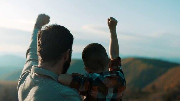 父亲抱着儿子他们在山顶上举起双手