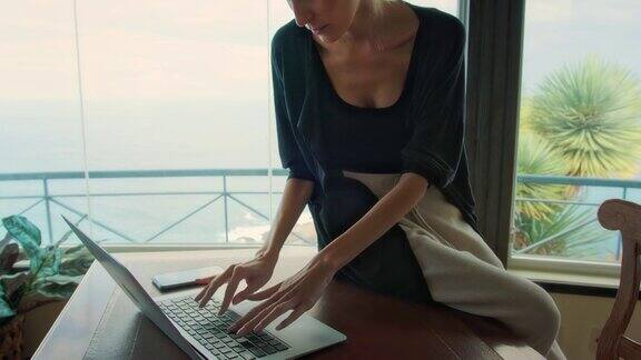在全景窗旁工作的女人使用笔记本电脑喝咖啡欣赏壮丽的海景