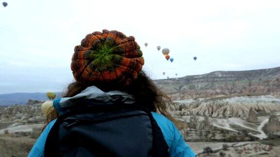 在土耳其卡帕多西亚的戈雷米一个年轻的女孩正在观看热气球在红色和玫瑰山谷飞行