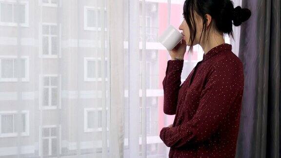 一位年轻女子正站在窗边喝咖啡