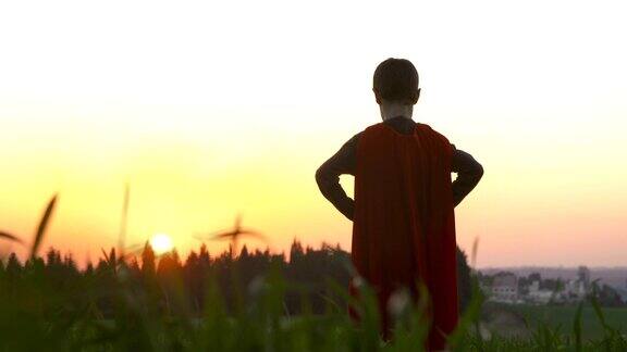一个男孩披着超级英雄斗篷在夕阳下的绿色田野里
